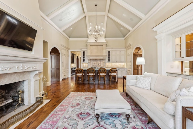living area with a high end fireplace, arched walkways, an inviting chandelier, and high vaulted ceiling