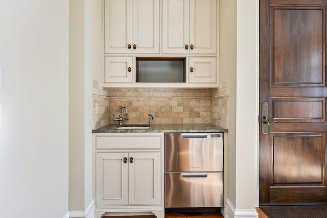 bar featuring backsplash, wet bar, refrigerator, a sink, and baseboards