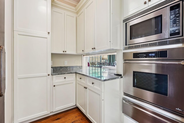 kitchen with dark wood-style flooring, appliances with stainless steel finishes, stone countertops, white cabinets, and a warming drawer