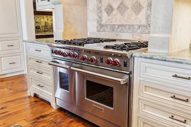 kitchen featuring decorative backsplash, light wood finished floors, light stone countertops, and range with two ovens
