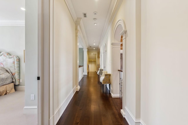 corridor featuring decorative columns, visible vents, baseboards, ornamental molding, and dark wood-type flooring