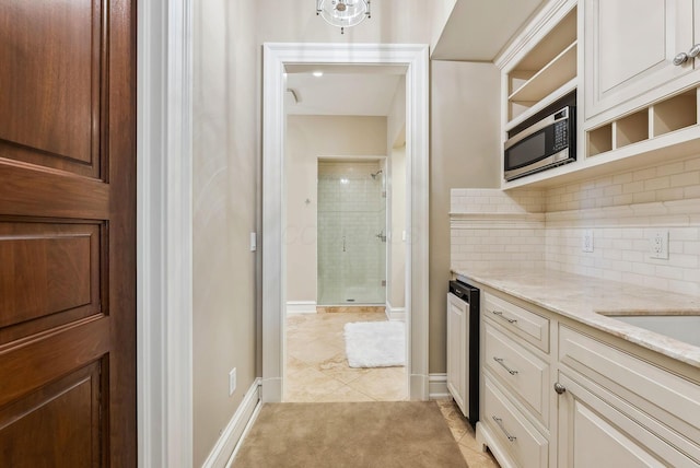 kitchen with backsplash, open shelves, light stone countertops, stainless steel microwave, and light tile patterned flooring