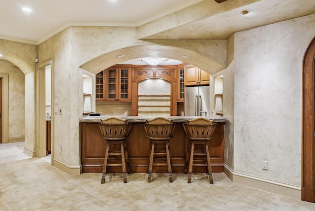 bar with light colored carpet, arched walkways, stainless steel refrigerator, and crown molding