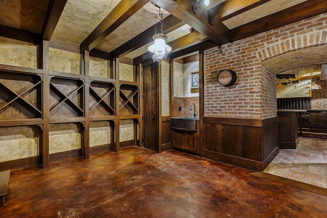 wine room featuring wainscoting, concrete flooring, wood walls, a sink, and an inviting chandelier