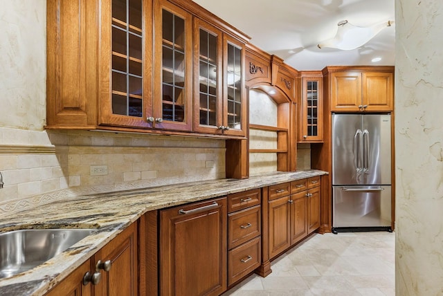 kitchen featuring light stone counters, tasteful backsplash, brown cabinetry, and stainless steel refrigerator