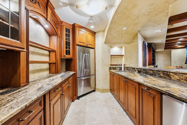 kitchen with brown cabinets, a sink, stone countertops, high end refrigerator, and glass insert cabinets