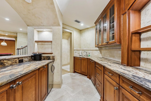 interior space featuring brown cabinetry, visible vents, tasteful backsplash, light stone countertops, and glass insert cabinets
