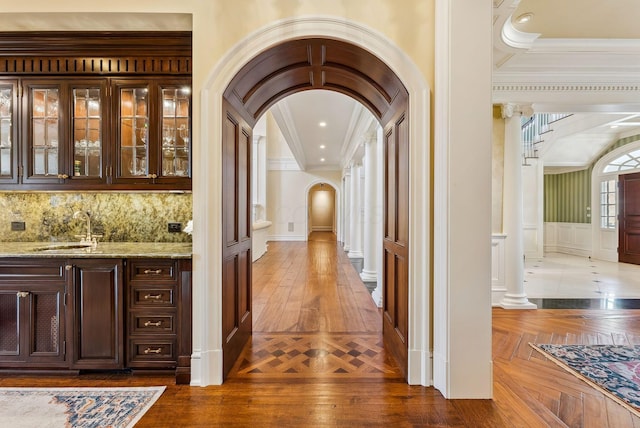 bar featuring crown molding, a sink, a decorative wall, arched walkways, and tasteful backsplash