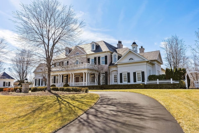 view of front of house with a porch, a chimney, a front yard, curved driveway, and fence