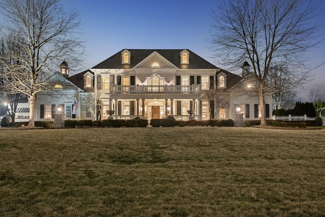 georgian-style home with fence, a porch, a front yard, a chimney, and a balcony