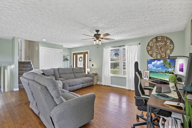 living area featuring wood-type flooring, baseboards, stairway, a textured ceiling, and a ceiling fan