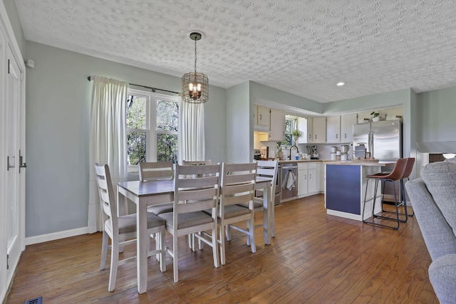 dining room featuring dark wood-type flooring, a textured ceiling, baseboards, and a chandelier