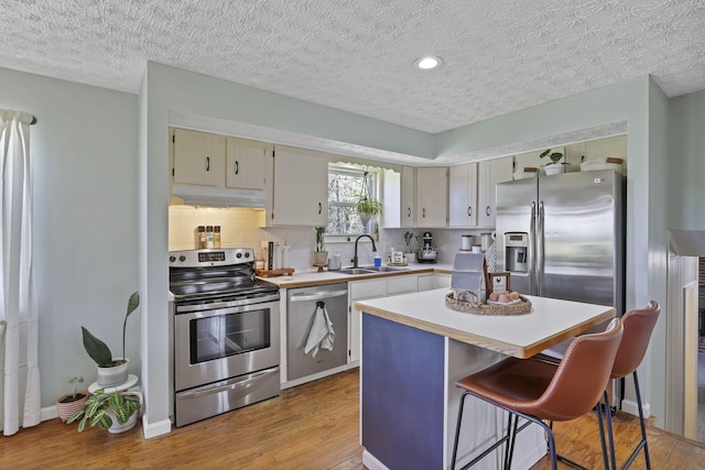 kitchen with appliances with stainless steel finishes, a sink, light wood-style floors, light countertops, and under cabinet range hood