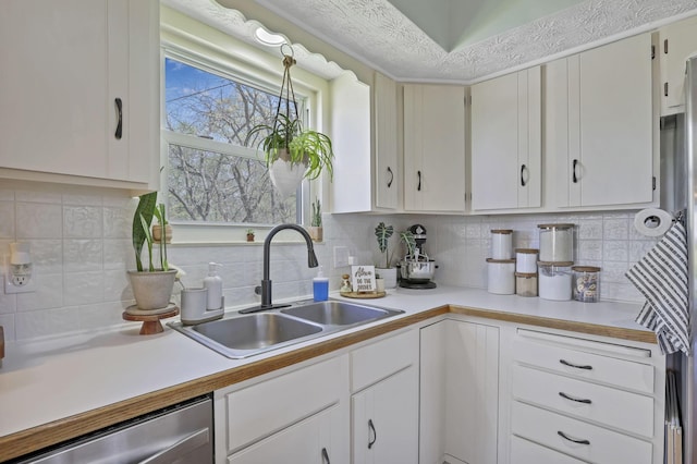 kitchen featuring white cabinets, a sink, dishwasher, light countertops, and tasteful backsplash