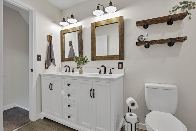 bathroom featuring a sink, baseboards, toilet, and double vanity