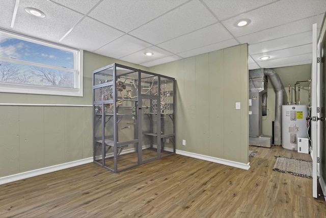 interior space with wood finished floors, baseboards, water heater, heating unit, and a decorative wall