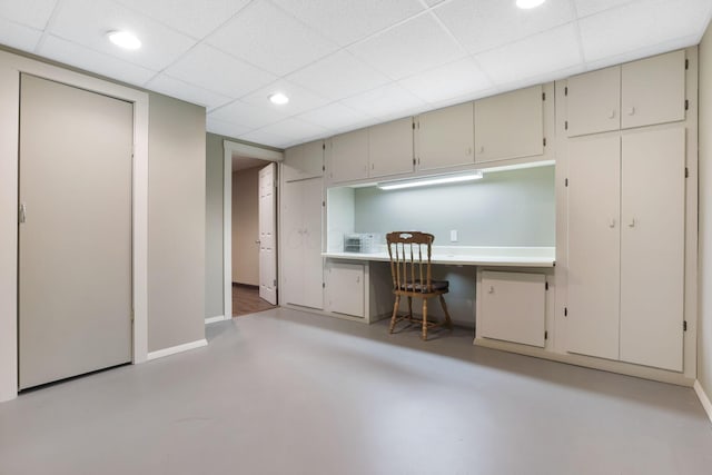 home office featuring a paneled ceiling, finished concrete flooring, built in study area, baseboards, and recessed lighting