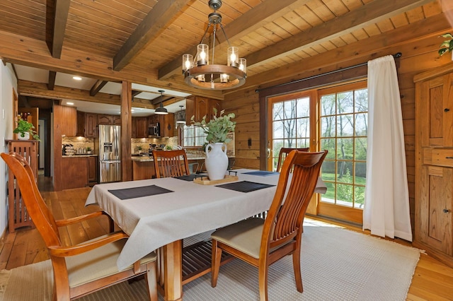 dining area with light wood-type flooring, beam ceiling, a healthy amount of sunlight, and an inviting chandelier