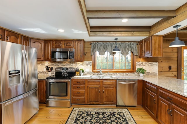 kitchen with appliances with stainless steel finishes, tasteful backsplash, light stone countertops, light wood-type flooring, and a sink