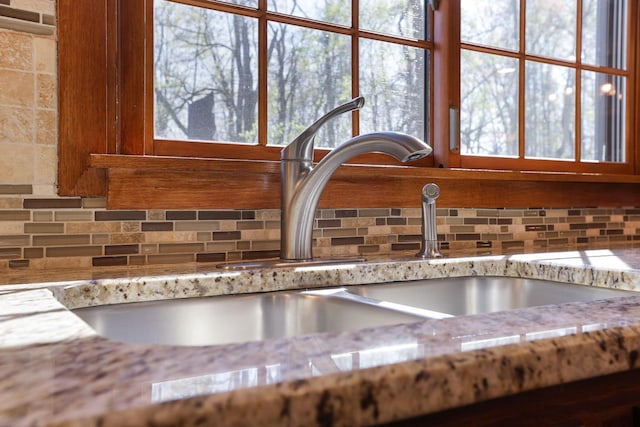 room details featuring a sink, decorative backsplash, and light stone countertops