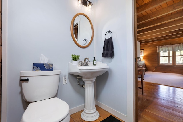 half bathroom with hardwood / wood-style flooring, wood walls, baseboards, beamed ceiling, and toilet
