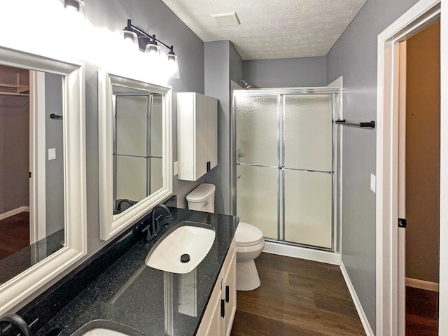 full bathroom featuring a sink, toilet, a textured ceiling, wood finished floors, and a stall shower