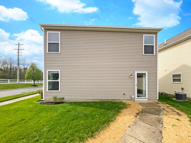 rear view of property featuring a lawn, central AC, and fence