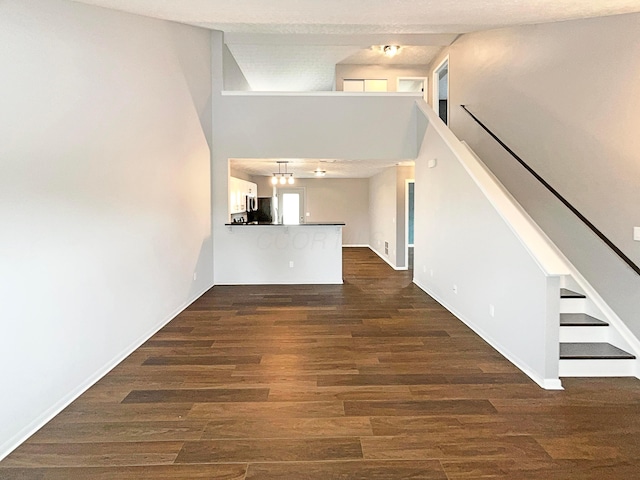 unfurnished living room featuring stairs, baseboards, and dark wood-style floors