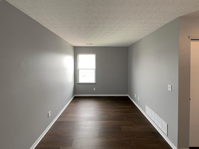 unfurnished room with visible vents, a textured ceiling, dark wood-style flooring, and baseboards
