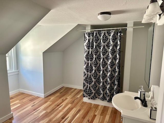 full bathroom with wood finished floors, a sink, curtained shower, a textured ceiling, and lofted ceiling
