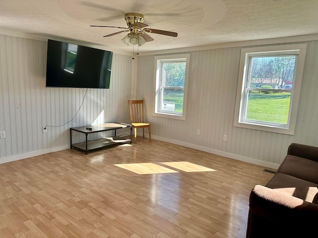 living area with a textured ceiling, a ceiling fan, a wealth of natural light, and light wood-type flooring