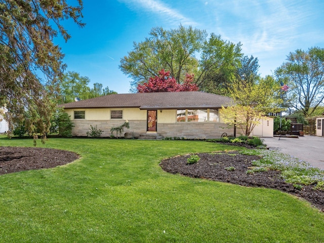 ranch-style house with an attached garage, a front lawn, stone siding, entry steps, and driveway