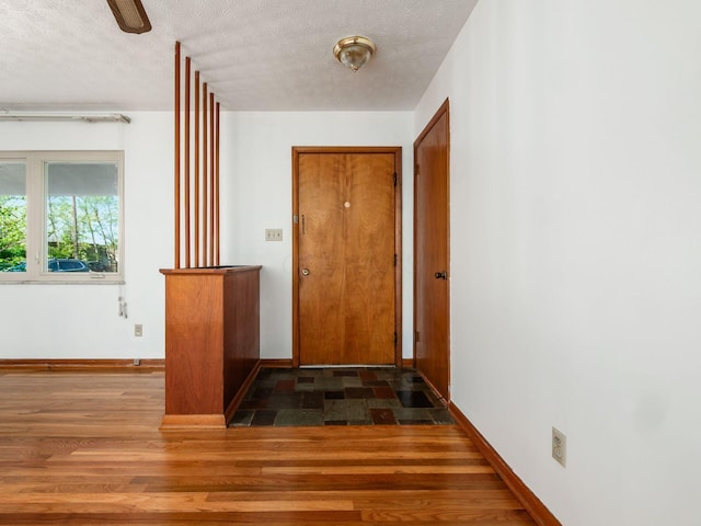 hall featuring baseboards, a textured ceiling, and wood finished floors