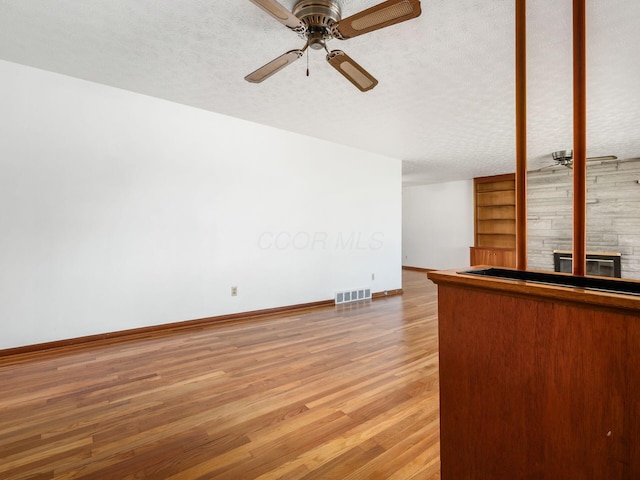 unfurnished living room featuring ceiling fan, a textured ceiling, baseboards, wood finished floors, and visible vents