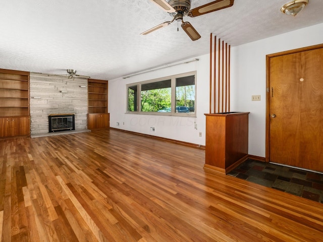 unfurnished living room featuring baseboards, a stone fireplace, a textured ceiling, and wood finished floors