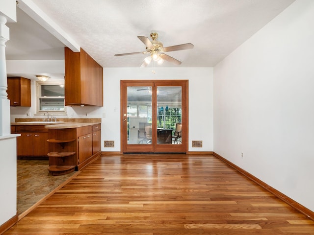 unfurnished dining area featuring baseboards, ceiling fan, light wood finished floors, and ornate columns