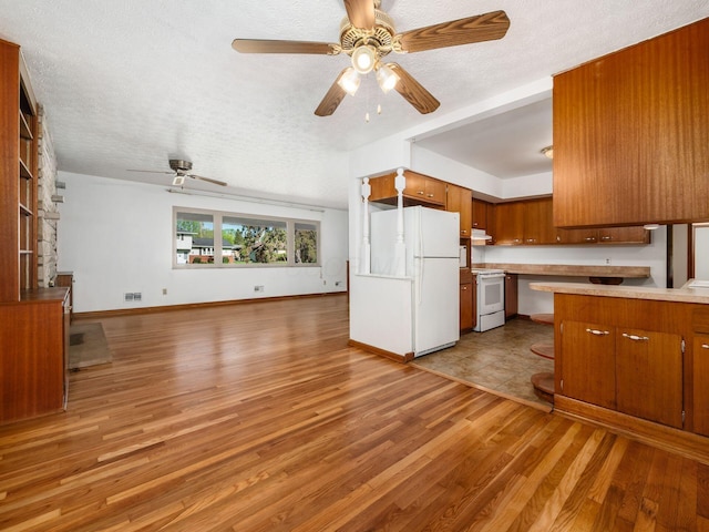 kitchen with light countertops, brown cabinetry, white appliances, and open floor plan