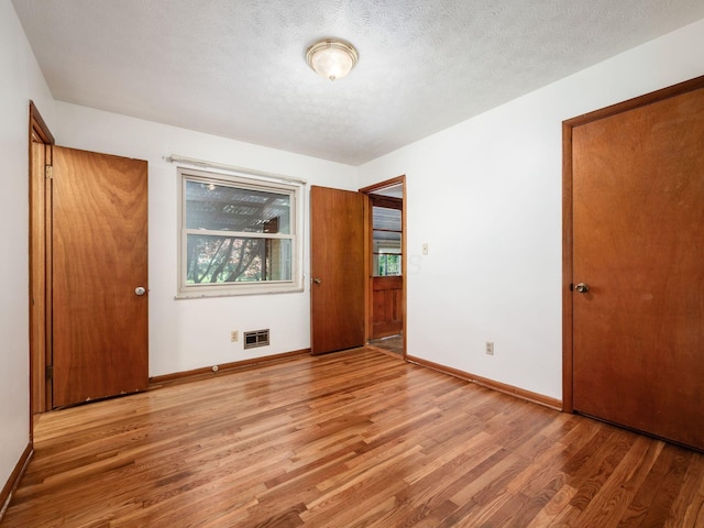 interior space with visible vents, a textured ceiling, light wood-style flooring, and baseboards