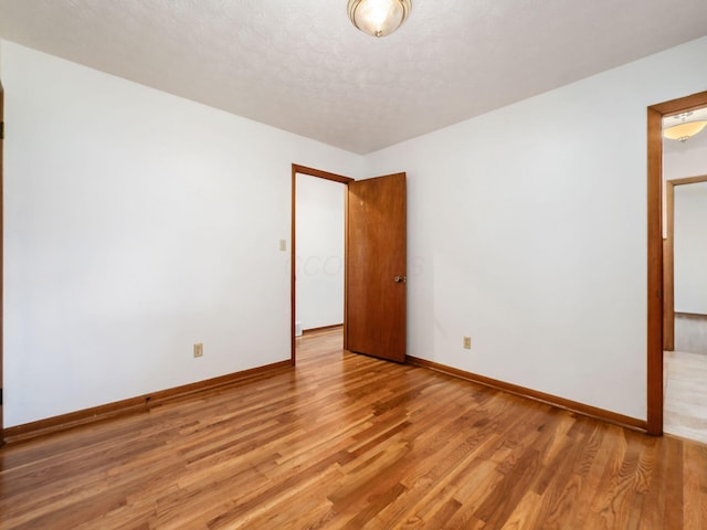 unfurnished bedroom featuring baseboards, light wood finished floors, and a textured ceiling