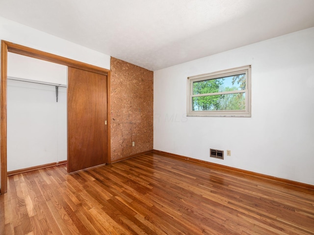 unfurnished bedroom featuring baseboards, visible vents, wood finished floors, and a closet