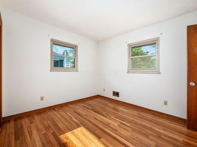 spare room featuring baseboards, visible vents, and wood finished floors