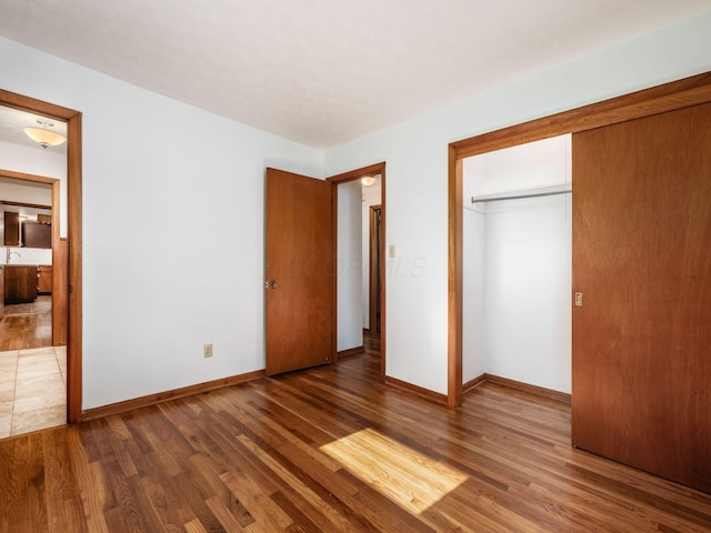 unfurnished bedroom with baseboards, a closet, wood finished floors, and connected bathroom