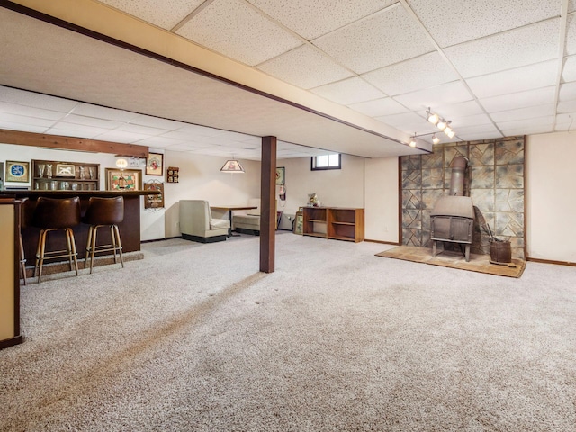 below grade area with carpet floors, baseboards, a paneled ceiling, and a wood stove