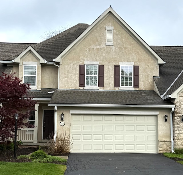 traditional-style house featuring a garage, aphalt driveway, and stucco siding
