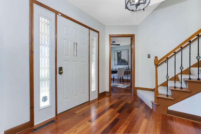 foyer featuring visible vents, baseboards, an inviting chandelier, wood-type flooring, and stairs