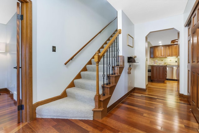 stairs with arched walkways, hardwood / wood-style flooring, and baseboards