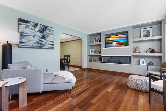 living room with baseboards, wood finished floors, built in features, and arched walkways