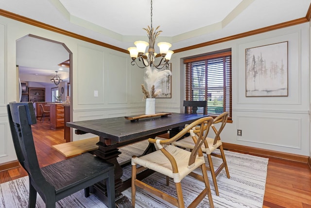 dining room featuring a decorative wall, a tray ceiling, arched walkways, wood finished floors, and a notable chandelier