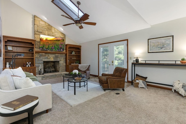 living room featuring vaulted ceiling with skylight, carpet, a fireplace, a ceiling fan, and french doors