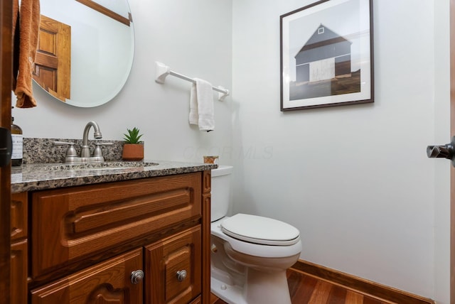 bathroom with toilet, vanity, wood finished floors, and baseboards